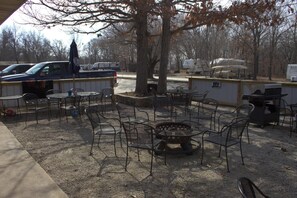 An outdoor seating area with metal chairs and a fire pit, surrounded by trees and parked vehicles. - Hidden Lake Resort (Warsaw)