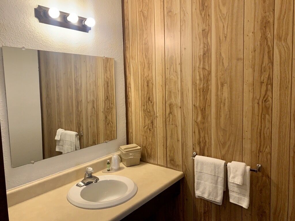 Een badkamer met een houten wand, een wastafel, een spiegel en twee handdoeken aan een rek.