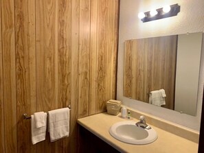 A bathroom with wooden panel walls, a white sink, a mirror, and two white towels hanging on hooks. - Hidden Lake Resort (Warsaw)