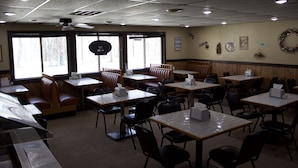 Un restaurant avec des banquettes et des tables, de grandes fenêtres et un ventilateur au plafond.
