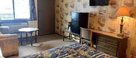 A hotel room with a bed, a desk, a chair, a television, and a window with curtains.