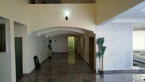 A spacious, well-lit hallway with a high ceiling and an arched structure. There are potted plants along the sides and a patterned wall on the right. - Water Ripples Hotel (Lekki)