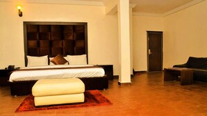 A hotel room with a large bed, a nightstand, a red rug, a dark upholstered chair, and a door. - Water Ripples Hotel (Lekki)