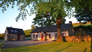 A traditional stone house with a red door, a chimney, and a large tree in front. - Mc Courts Cottage, Mourne Mountains  (HILLTOWN)