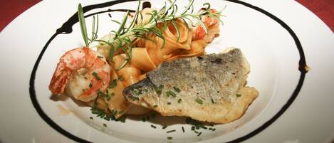 A plate of food with shrimp, pasta, and fish, garnished with herbs.