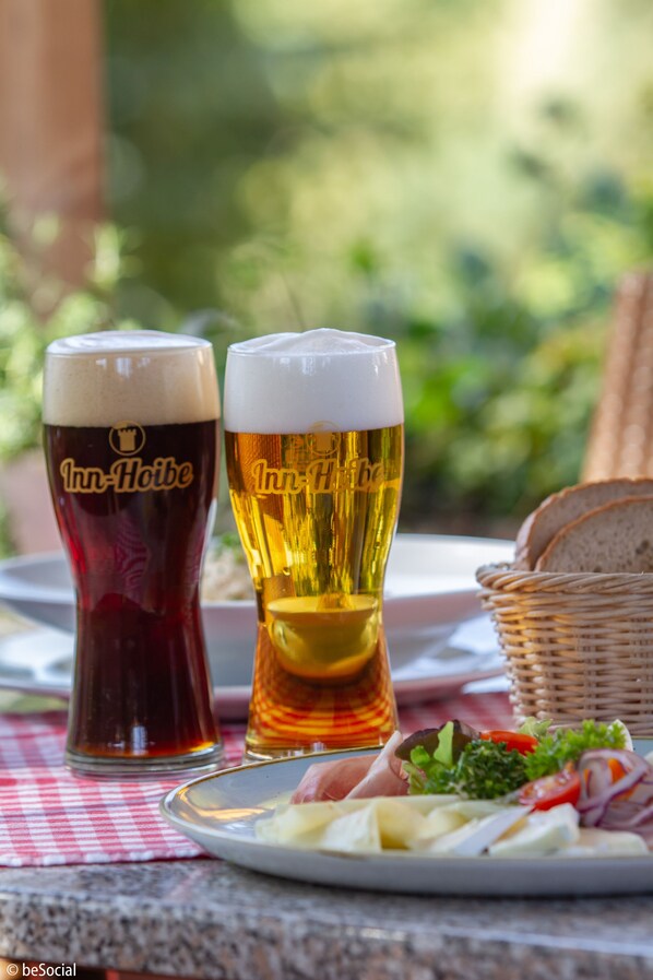 Two glasses of beer on a table with a plate of food and a basket.