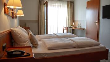 Habitación de hotel con cama doble, lámparas de noche, escritorio con lámpara, una silla y televisor montado en la pared.