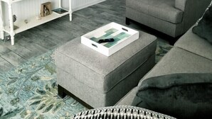 Ein Wohnzimmer mit blauer Akzentwand, einem Flachbildfernseher, einem grauen Sofa, einem weißen Konsolentisch und einem gemusterten Teppich.