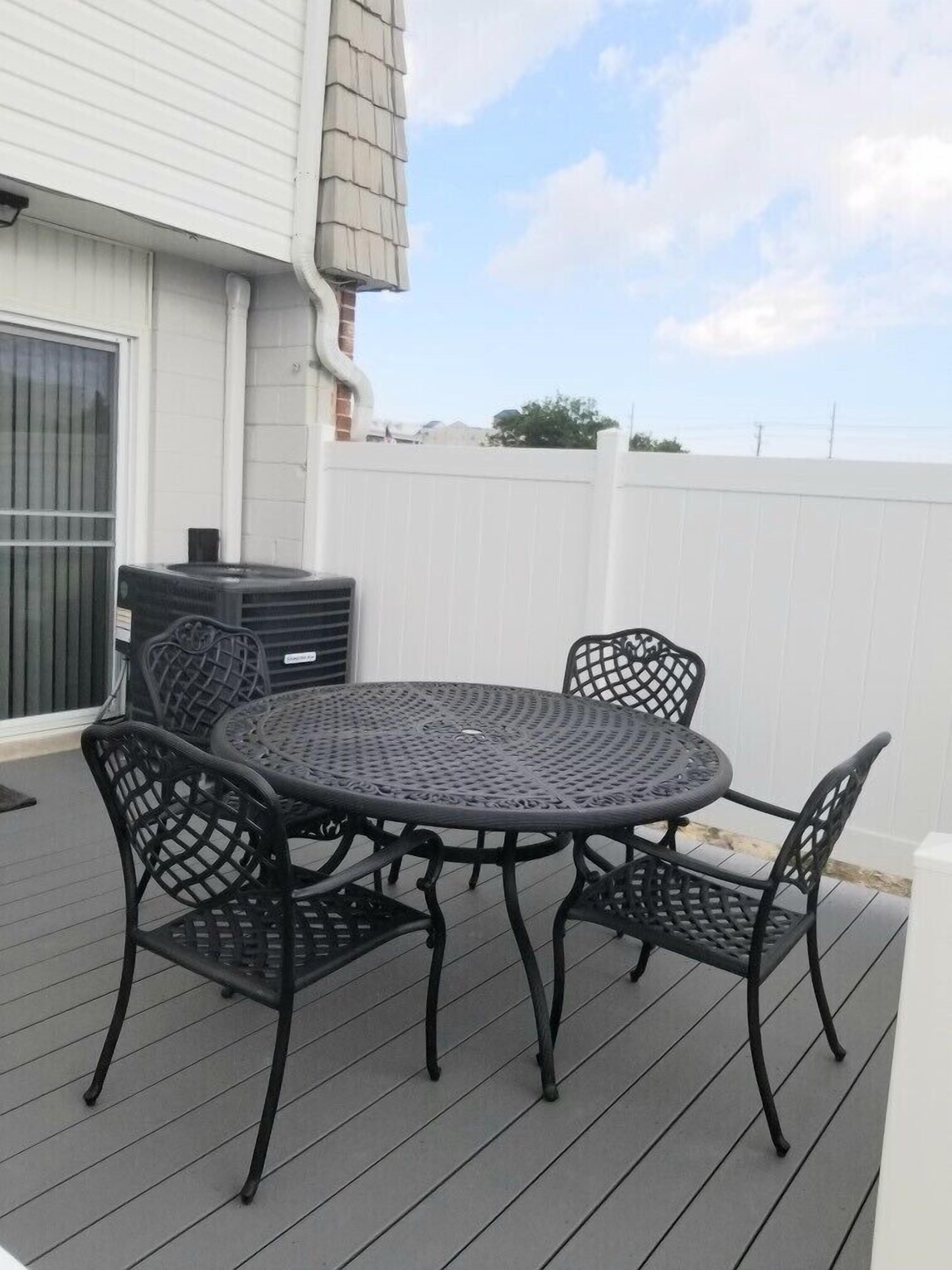 Een terras met een ronde tafel, vier stoelen, een prullenbak en een witte schutting.