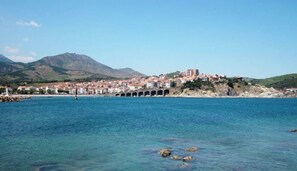 A coastal town with a prominent bridge, clear blue waters, and a mountainous backdrop.