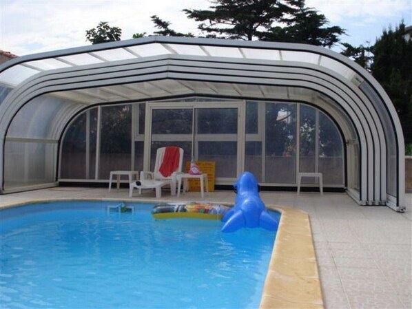 A covered swimming pool with a glass enclosure, a blue inflatable toy, and a red towel on a chair. - APARTMENT T3 in villa 4 faces in BANYULS on sea PARKING CLOS (Banyuls-sur-Mer)