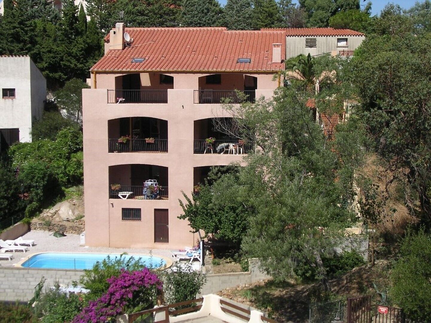 Un immeuble à plusieurs étages doté de balcons, d’une piscine et d’une végétation luxuriante.