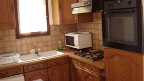 A kitchen with wooden cabinets, a microwave, a stove, and a window with curtains. - APARTMENT T3 in villa 4 faces in BANYULS on sea PARKING CLOS (Banyuls-sur-Mer)