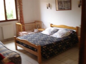 A bedroom with a wooden bed, a nightstand, a crib, and a window with curtains.