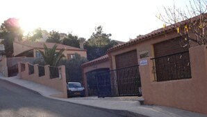 A residential street with a parked car, a gated garage, and a building with a tiled roof. - APARTMENT T3 in villa 4 faces in BANYULS on sea PARKING CLOS (Banyuls-sur-Mer)