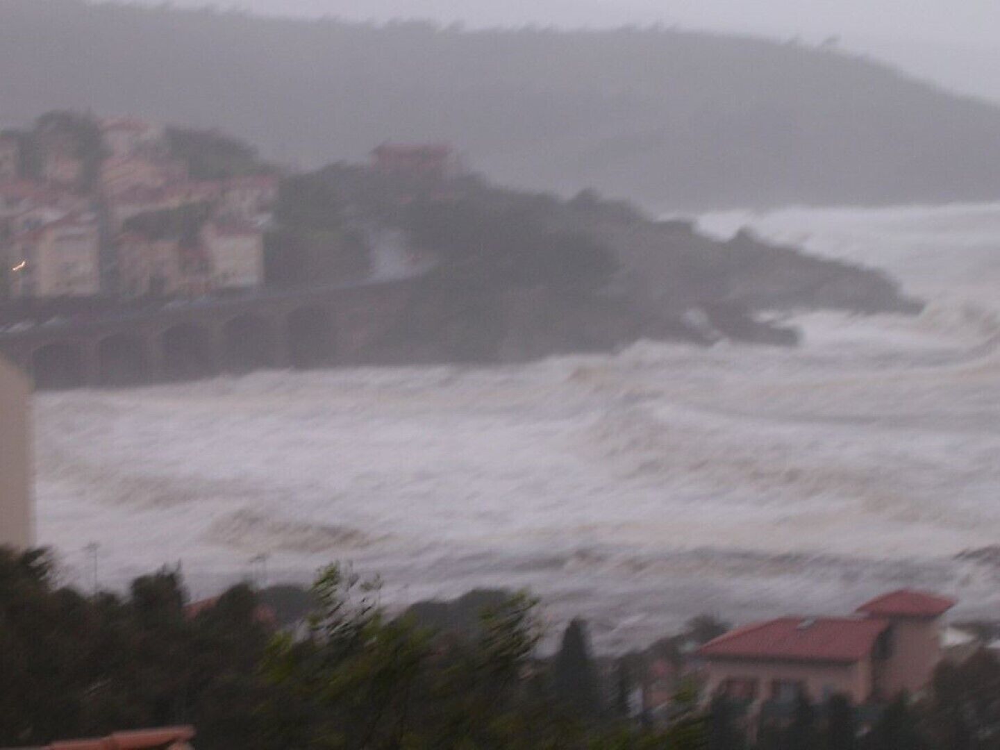 A coastal view with a building on the left and a turbulent sea in the foreground.
