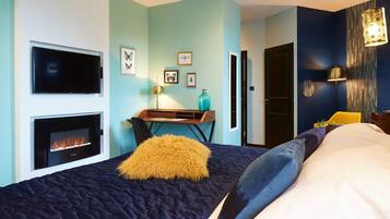 A modern bedroom with a large bed, a fireplace, a desk, and a chair.