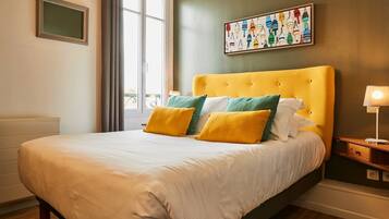 Una habitación de hotel con una cama grande, una mesita de noche con lámpara, una ventana con cortinas y una obra de arte en la pared.