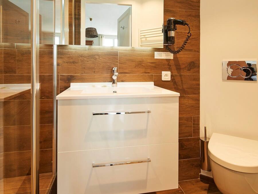 A bathroom with a white sink, mirror, and toilet. There is a towel rack on the wall and a trash can next to the toilet.