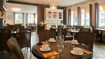 A dining area with wicker chairs and tables, a globe, and a sign reading "NOIR MOUTIER".