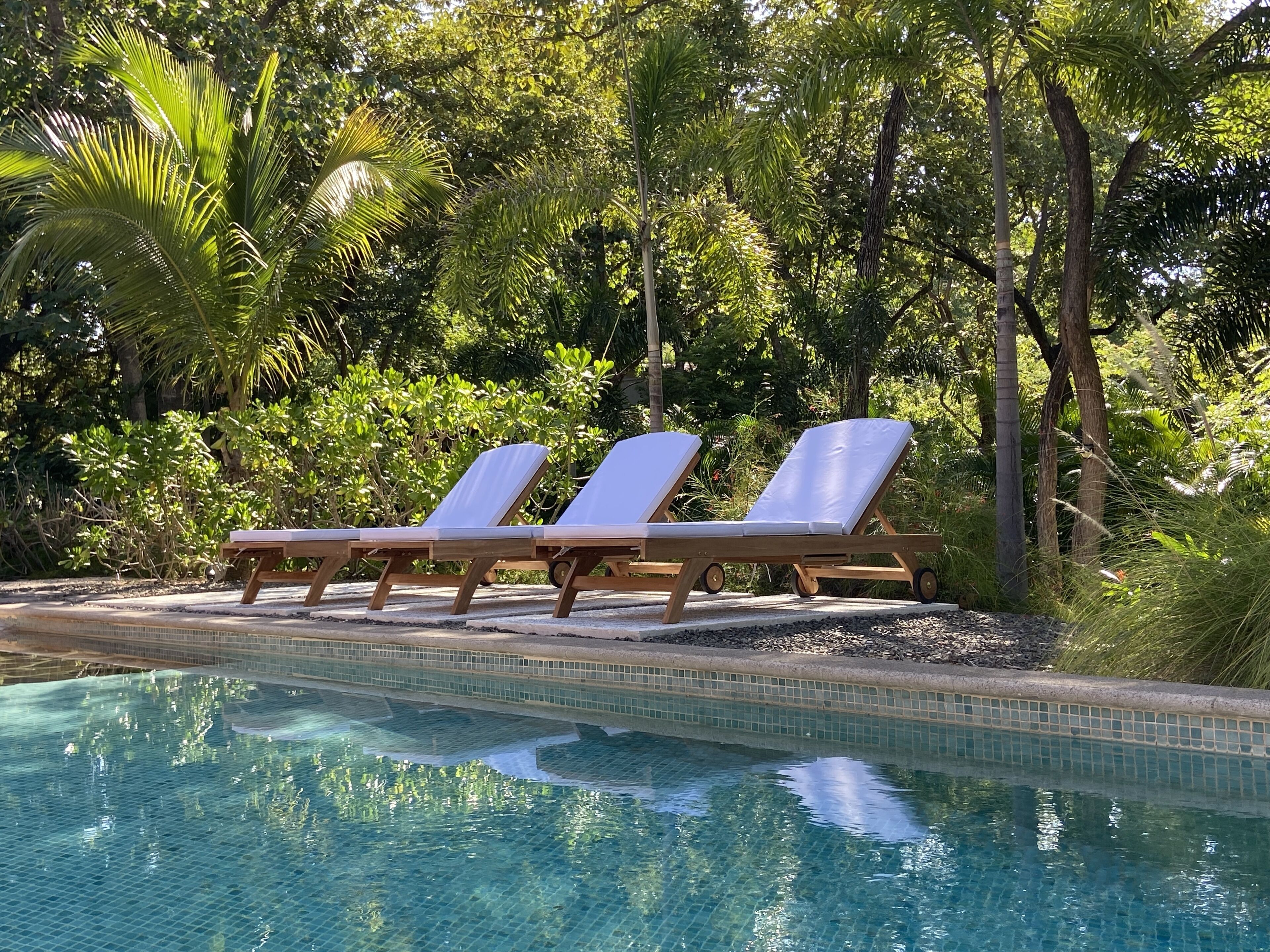 A pool area with three sun loungers and a tiled pool.