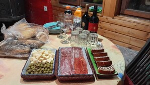 Uma mesa com diversos alimentos, incluindo queijo, azeitonas e embutidos, além de garrafas de bebidas e copos.
