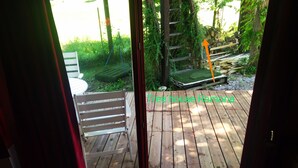 Um deck de madeira com uma cadeira e uma pequena mesa, cercado por vegetação e um cercado de madeira.
