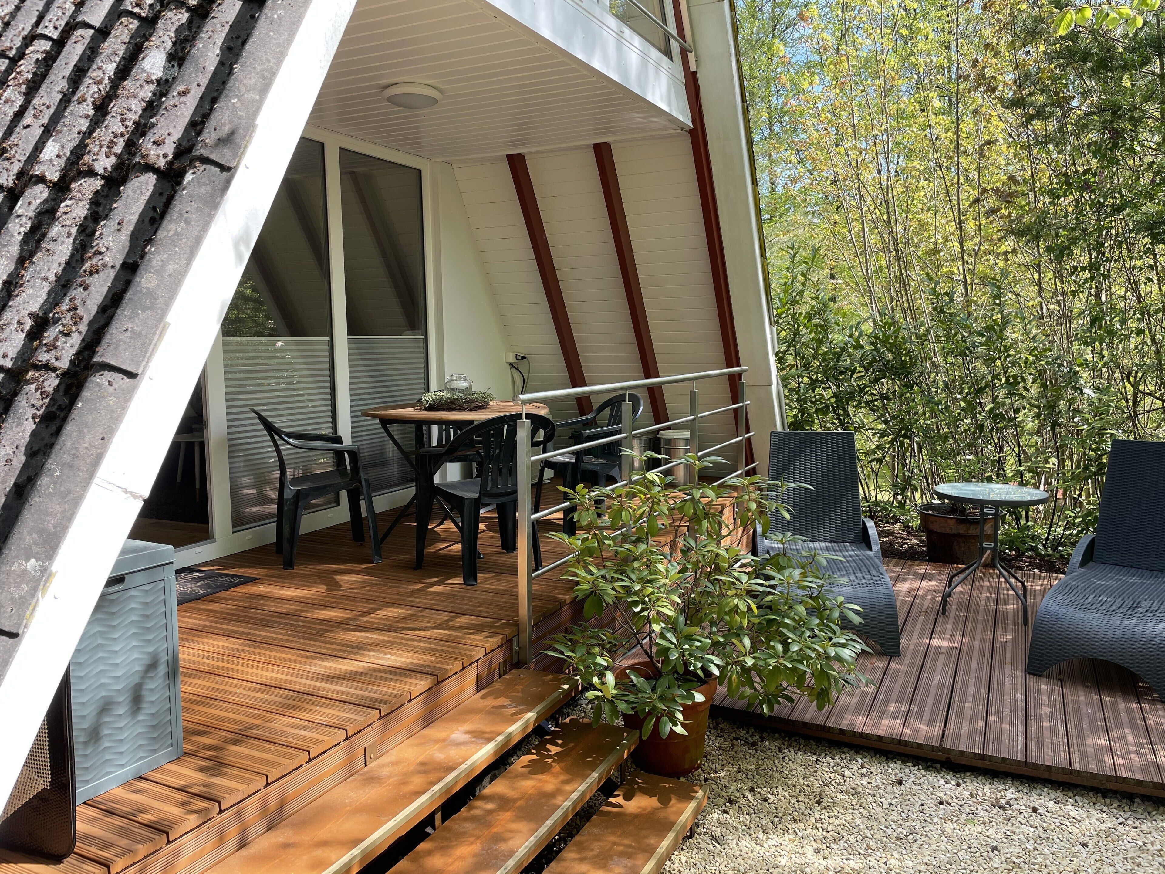 Une terrasse extérieure moderne, dotée d’une plateforme en bois, d’une table à manger avec des chaises, et d’une petite table ronde également accompagnée de chaises.