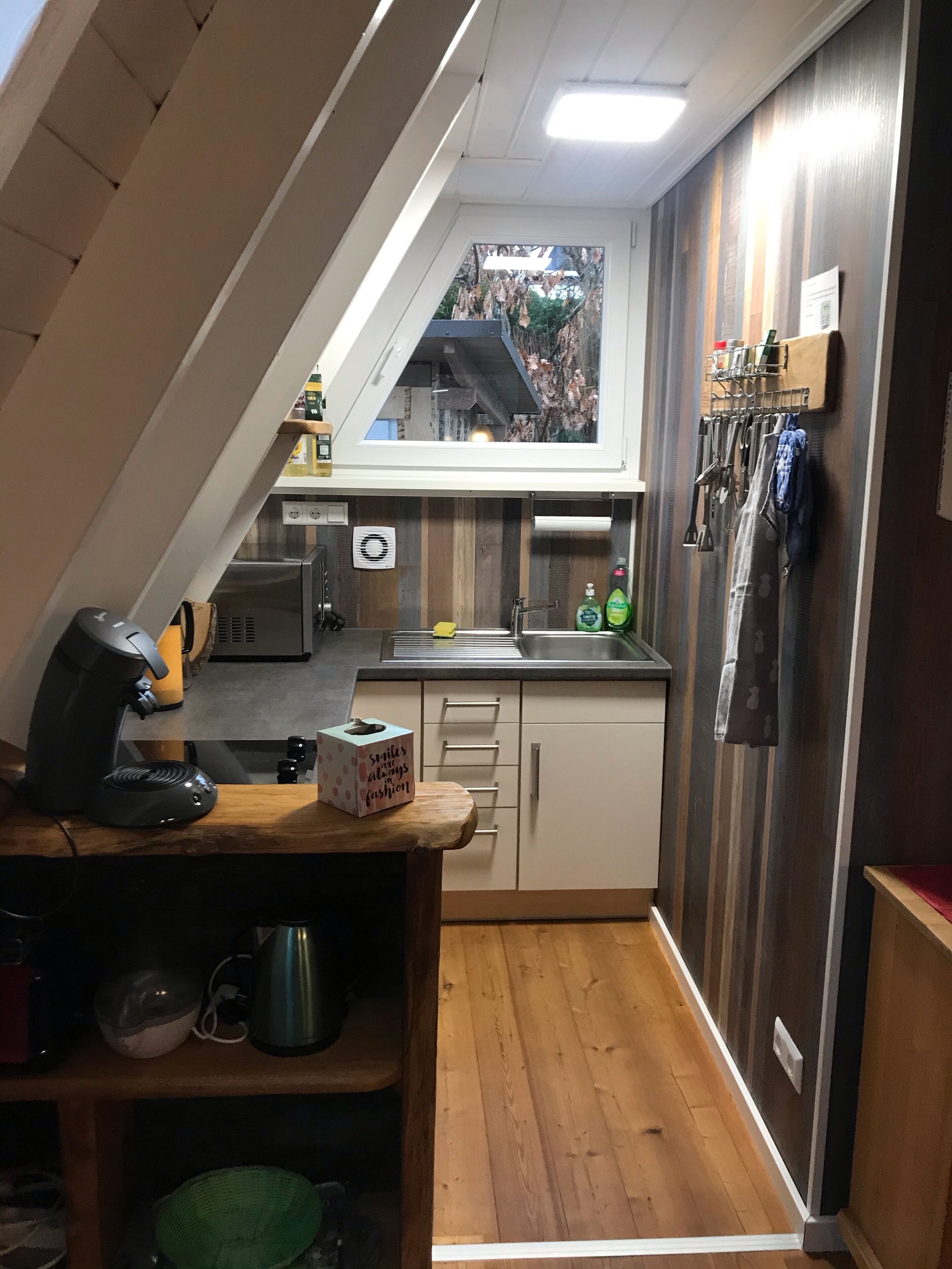 A compact kitchen with a window, a coffee machine, a kettle, and a sink.