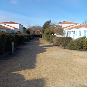 Un camino de grava conduce a una glorieta de madera en una zona residencial con casas blancas y contraventanas azules.