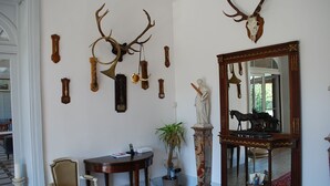 A room with a large mirror, a statue, and various wall-mounted antlers and horns. - Chateau 150kms south of Paris for 15 people (Cerdon)