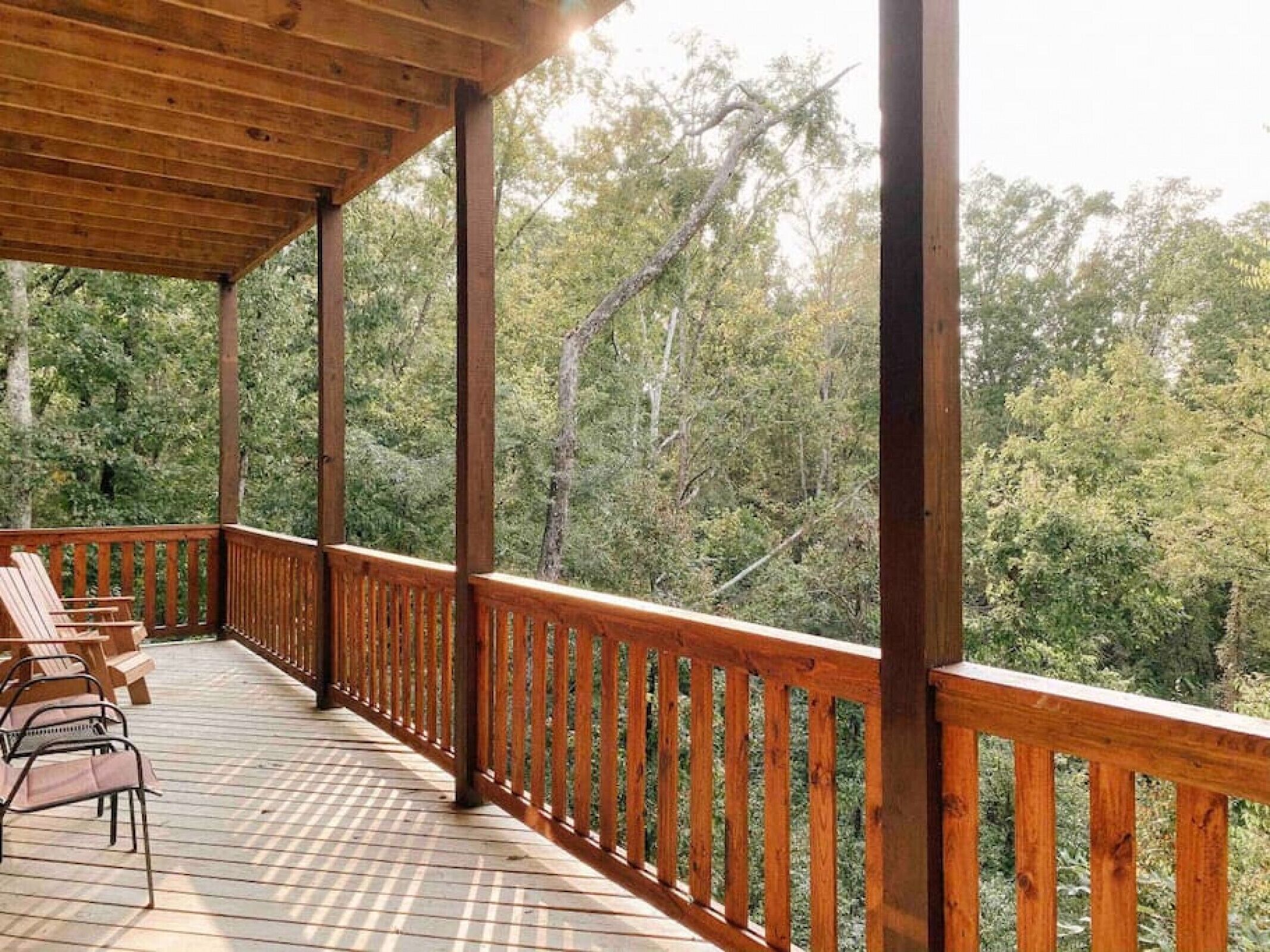 A wooden deck with a railing, surrounded by trees.
