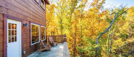 A wooden cabin with a deck, surrounded by autumn foliage.