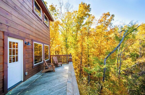 A wooden cabin with a deck, surrounded by autumn foliage. - Splash of Moonshine - Heated Indoor Pool, Hot Tub, Arcade/Game Room (Pigeon Forge)