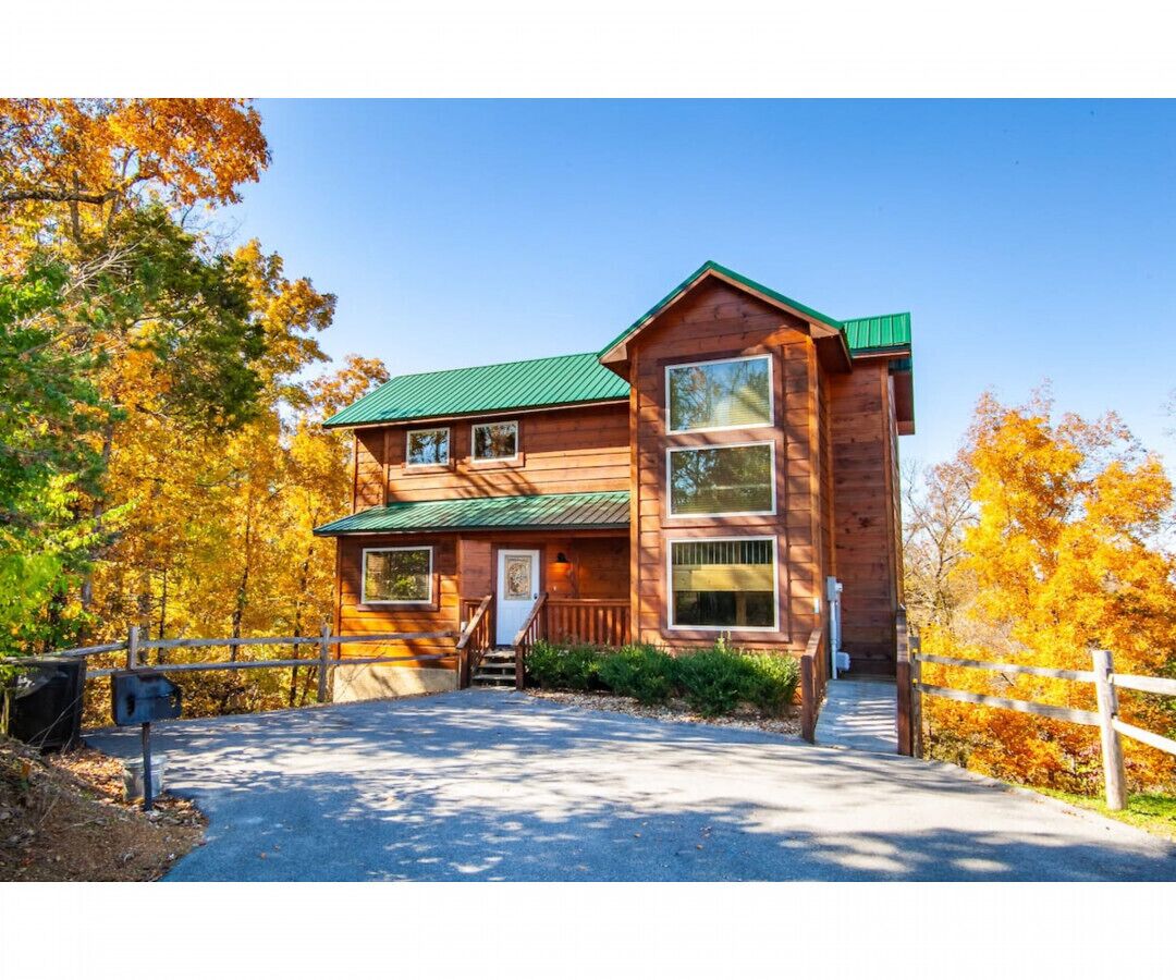 Une cabane en bois à deux étages, avec un toit vert, une véranda et une boîte aux lettres.