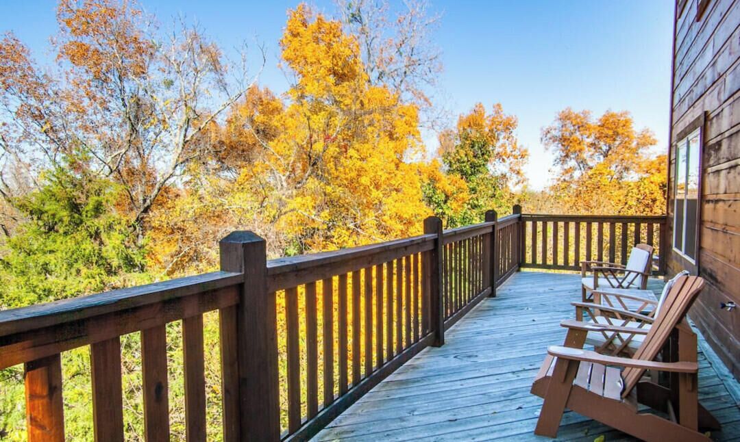 A wooden deck with a railing, surrounded by autumn foliage.