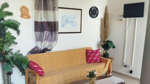 Un salon avec un canapé, une table basse, un téléviseur et une horloge au mur.