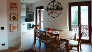 A dining area with a wooden table and chairs, a kitchen in the background, and a balcony with a view. - large and comfortable apartment in Courmayeur (Courmayeur)