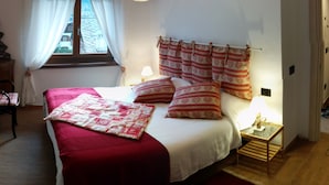 A bedroom with a bed, a bedside table, a lamp, a window with curtains, and a hanging light fixture. - large and comfortable apartment in Courmayeur (Courmayeur)