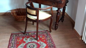 A corner room with a wooden chair, a small wooden table, a patterned rug, and a window with a decorative curtain. - large and comfortable apartment in Courmayeur (Courmayeur)