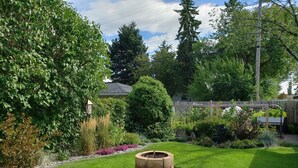 Ein gepflegter Garten mit einem runden Feuerkorb, üppigem Grün und einem Holzzaun.