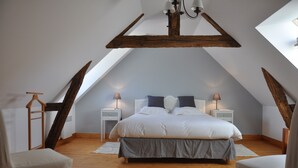 A bedroom with a sloped ceiling, wooden beams, a bed with white bedding, two bedside tables with lamps, and a wooden floor.