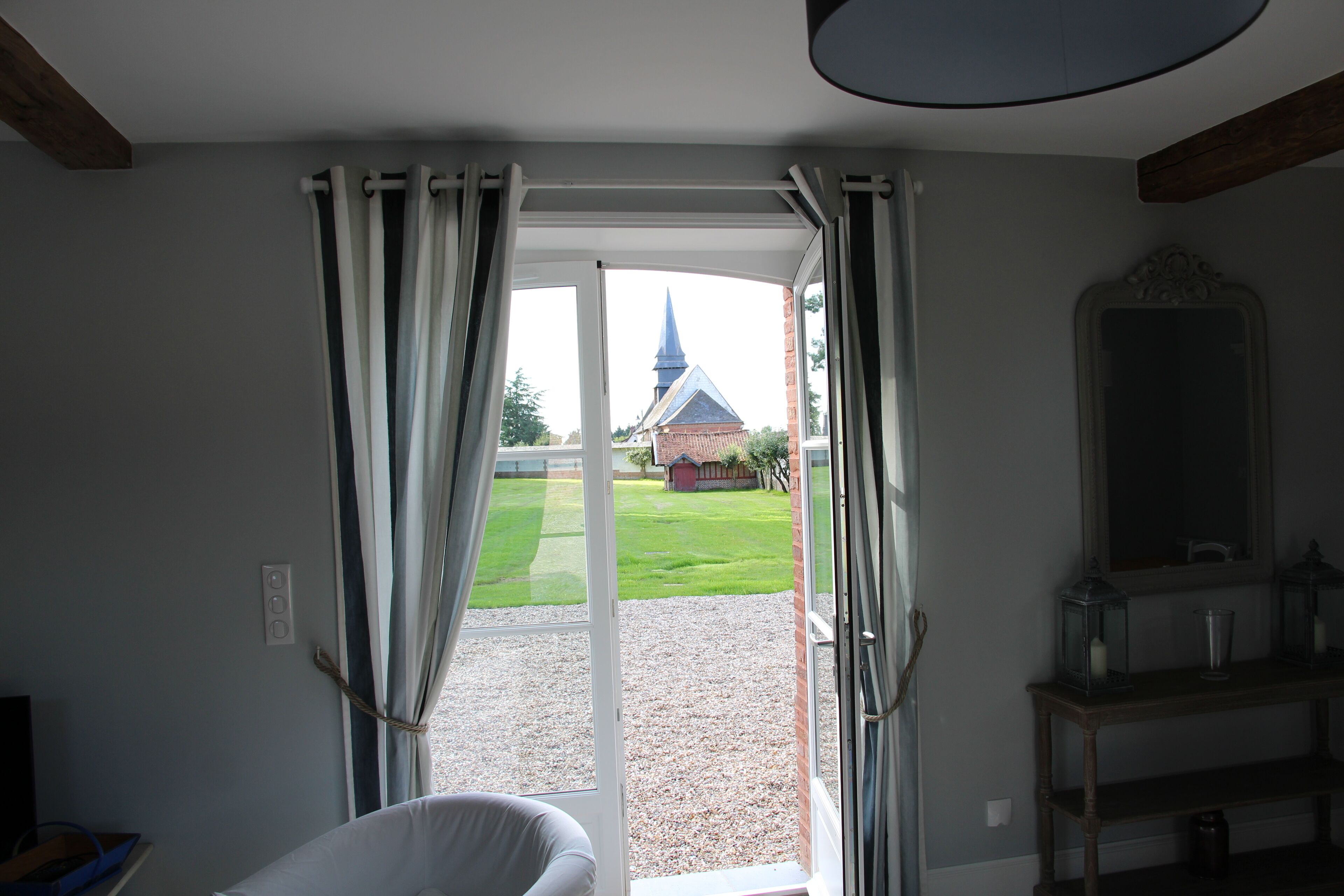 A room with a sliding glass door leading to a garden, a chair, a table with a lantern, and a mirror on the wall.