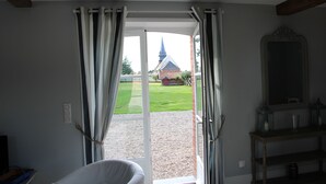 A room with a sliding glass door leading to a garden, a chair, a table with a lantern, and a mirror on the wall.