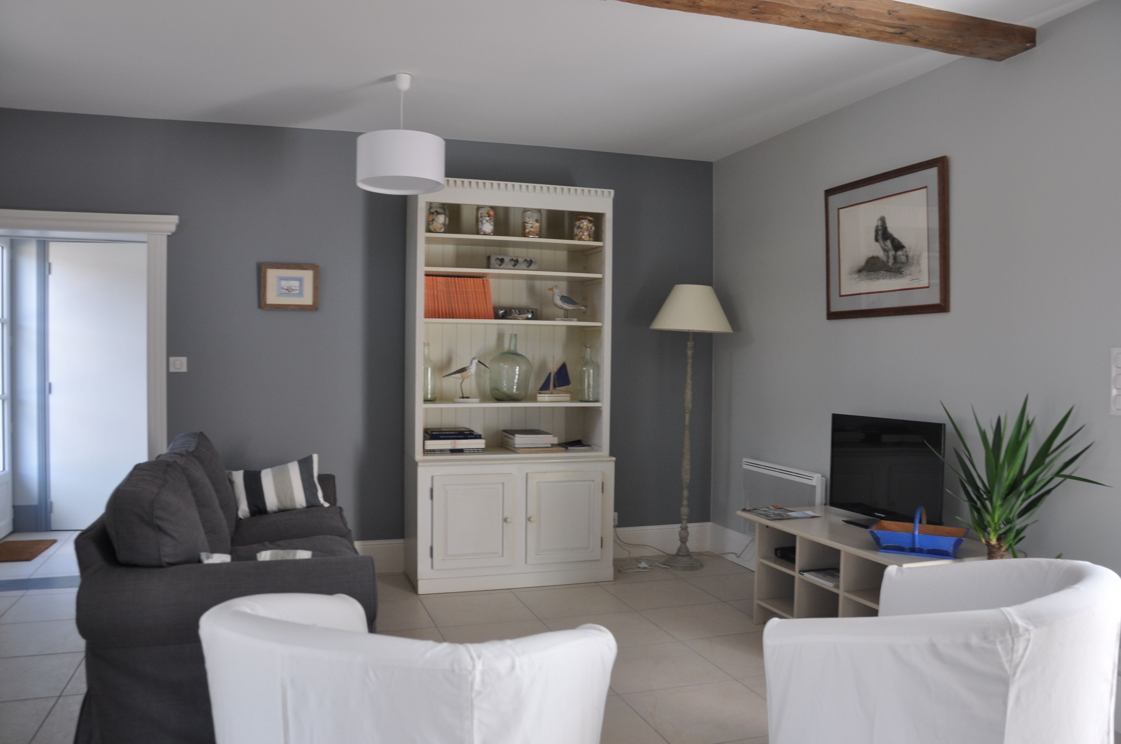 Een moderne woonkamer met een grijze bank, witte fauteuils, een witte kast met decoratieve objecten, een tv-meubel en een vloerlamp.
