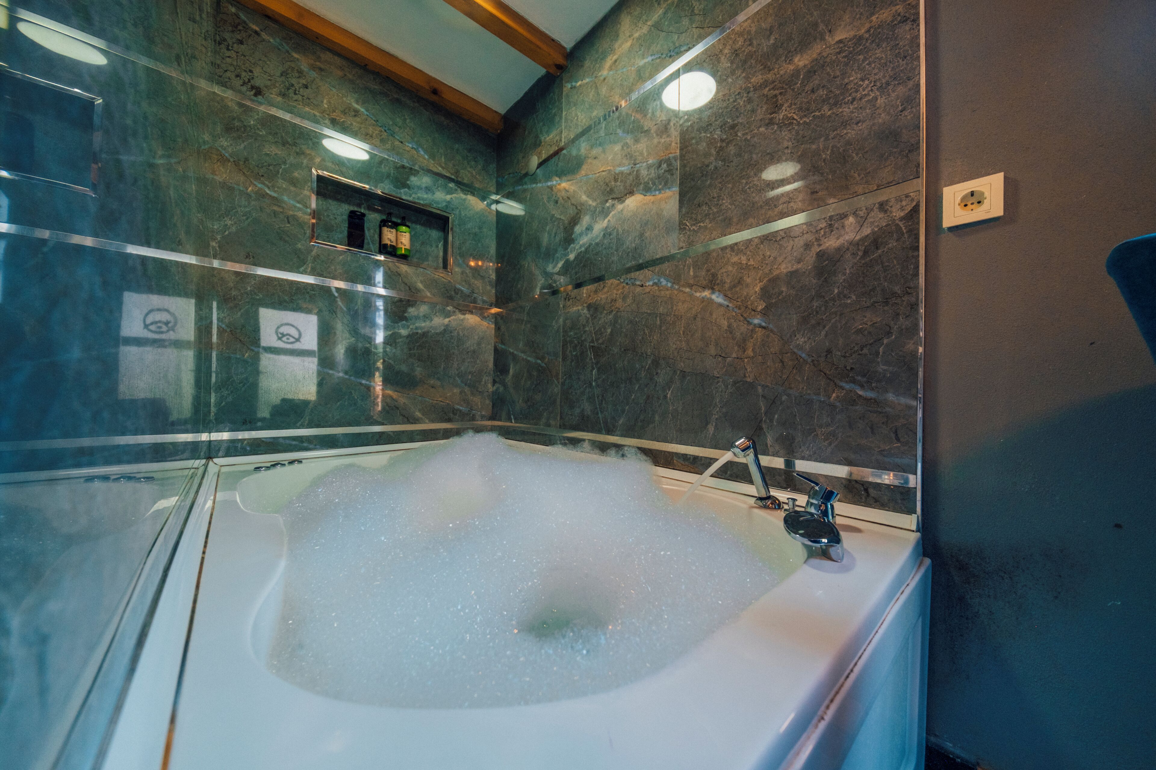 A modern bathroom with a glass-enclosed jacuzzi, marble walls, and a wooden ceiling.