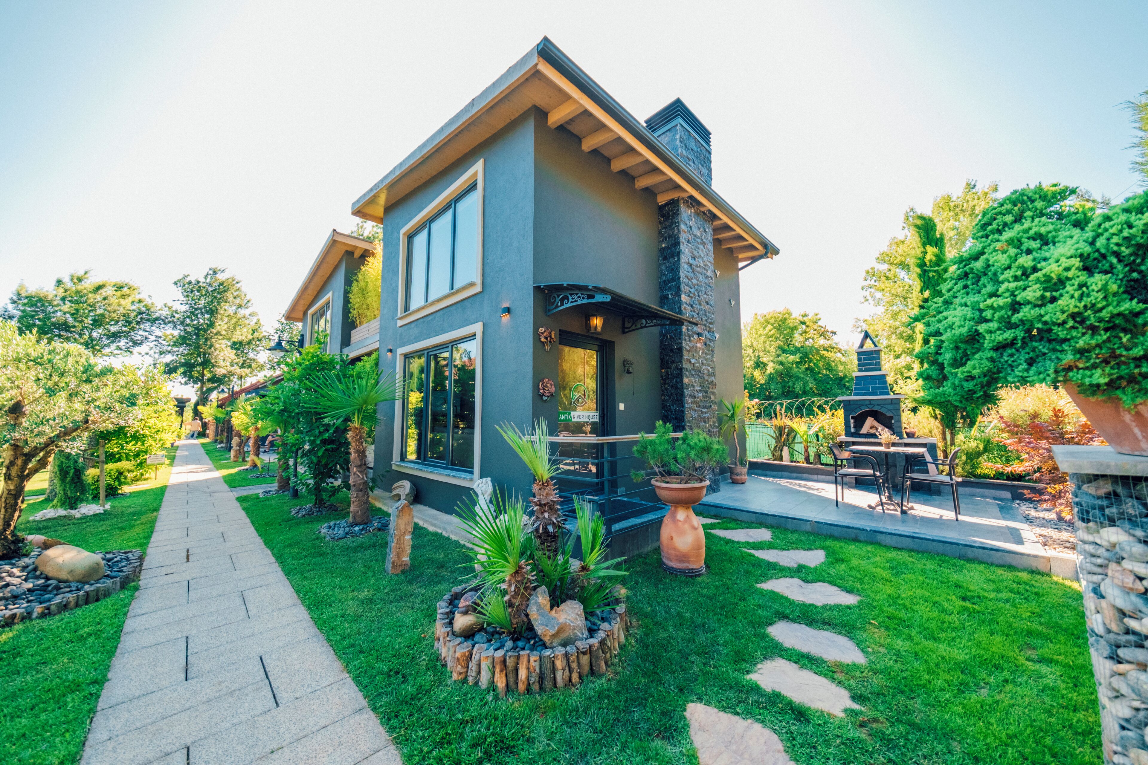 A modern two-story house with a stone fireplace, a paved walkway, and a well-maintained garden.