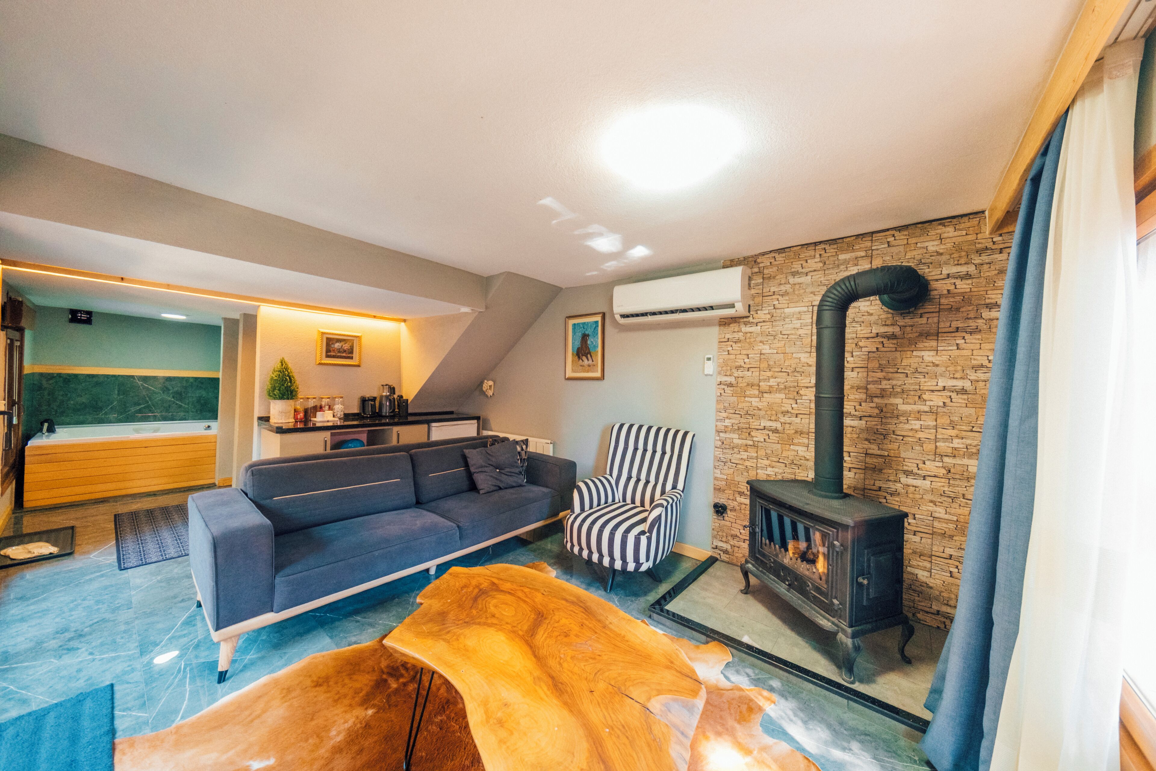 A modern living room with a sofa, a striped armchair, a wooden coffee table, and a stone wall with a fireplace.