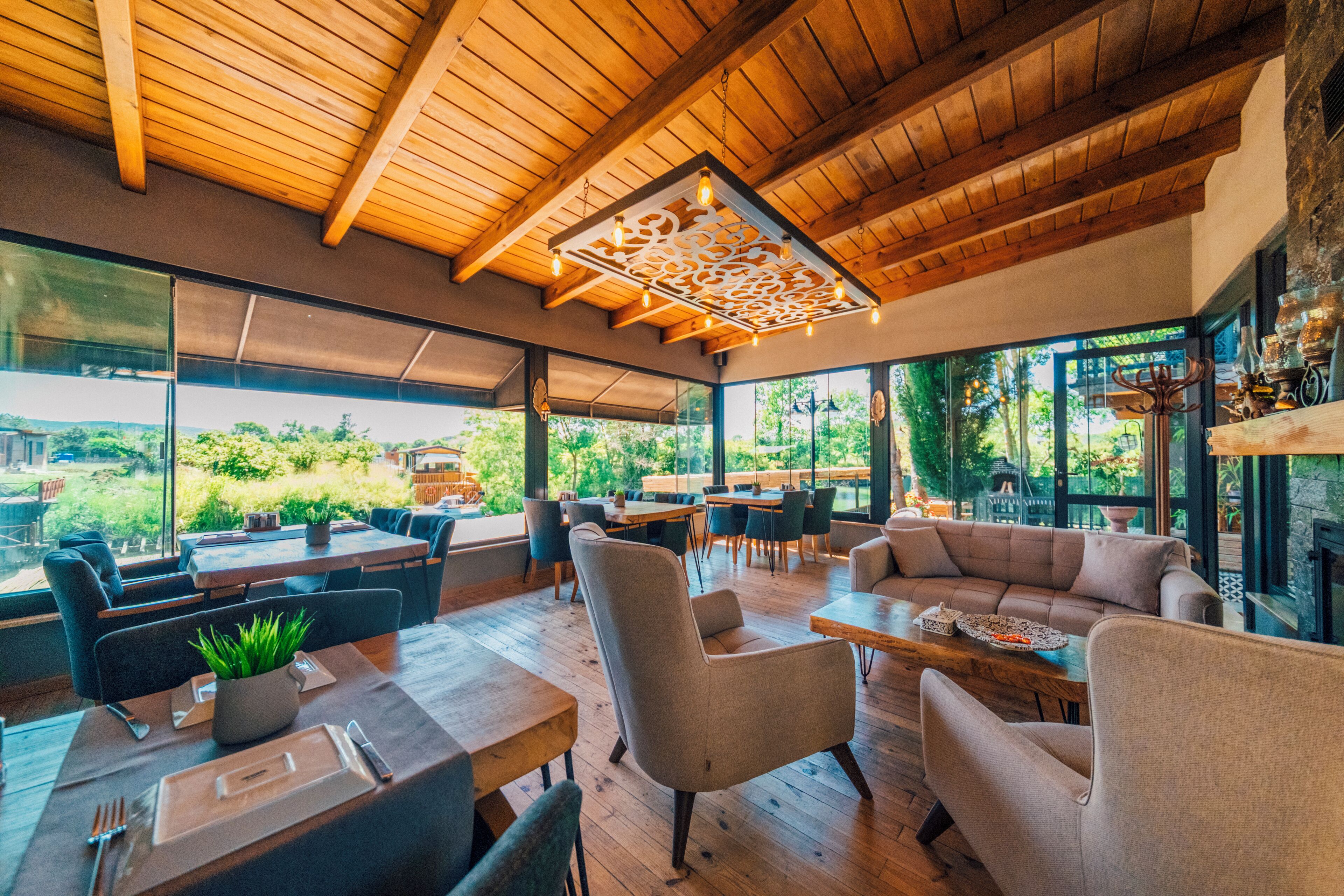 Un restaurante moderno con techos de madera, ventanas amplias y una variedad de opciones de asientos, incluidas mesas y sofás.