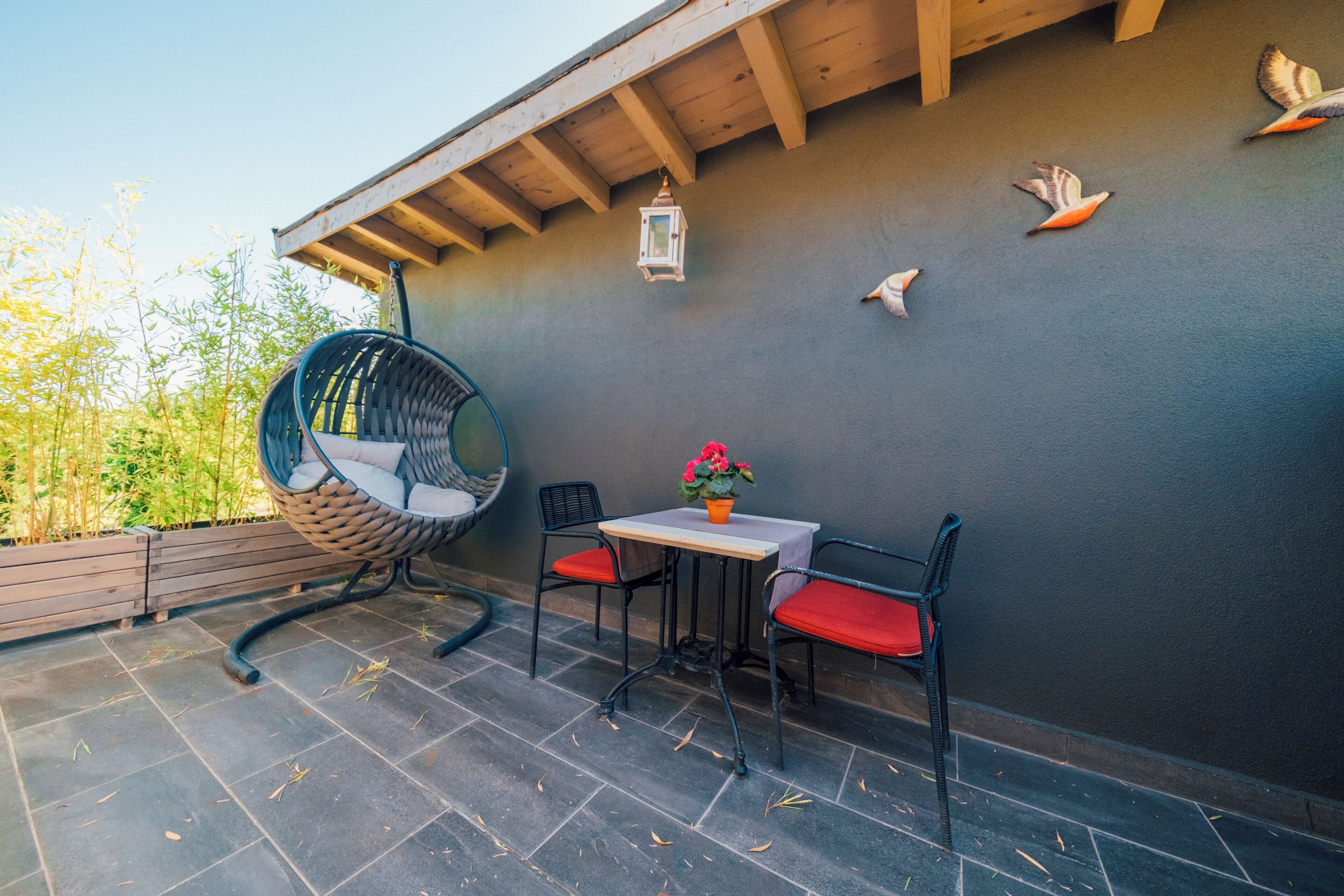 An outdoor patio with a swing chair, a table with chairs, and decorative wall art.